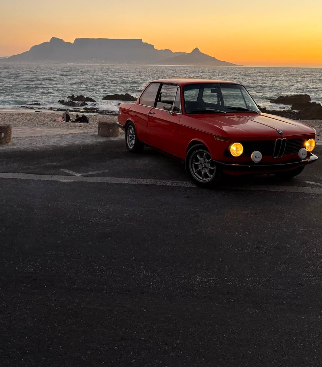 Red BMW 2002 by the Cape Town coast with Table Mountain at sunset
